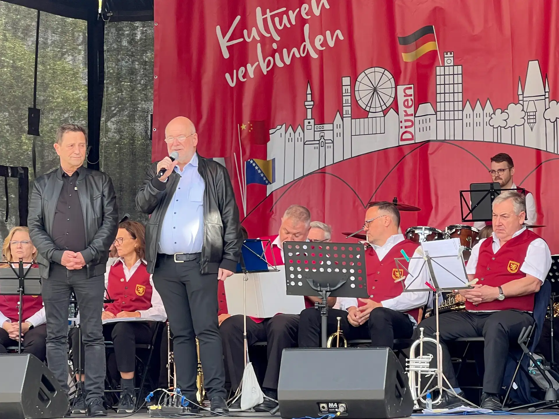 Personen stehen bei der Eröffnung einer Partnerschaftsmeile; im Hintergrund sind weitere Mitwirkende sowie der Veranstaltungsbereich zu erkennen.