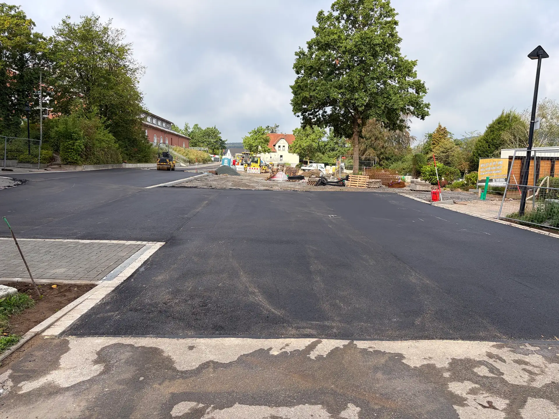 Baustelle auf einem Parkplatzgelände mit Erd- bzw. Arbeitsbereich im Vordergrund und Bauarbeiten im Hintergrund.