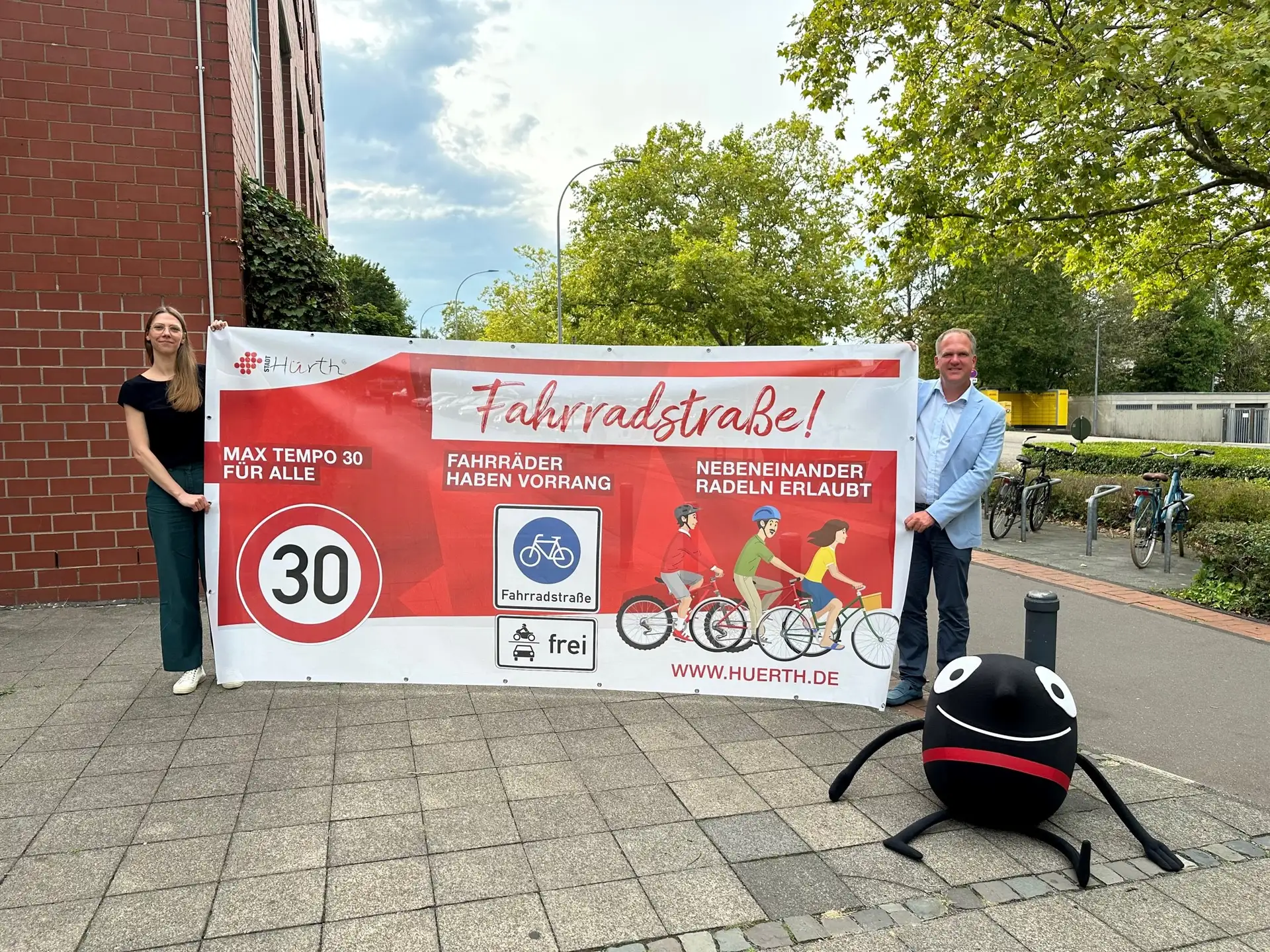 Bürgermeister Dirk Breuer und Mobilitätsmanagerin Romy Simke präsentieren die Bauzaunbanner, die im Rahmen der Europäischen Mobilitätswo- chen auf die Regeln der Hürther Fahrradstraßen aufmerksam machen sollen. © Stadt Hürth