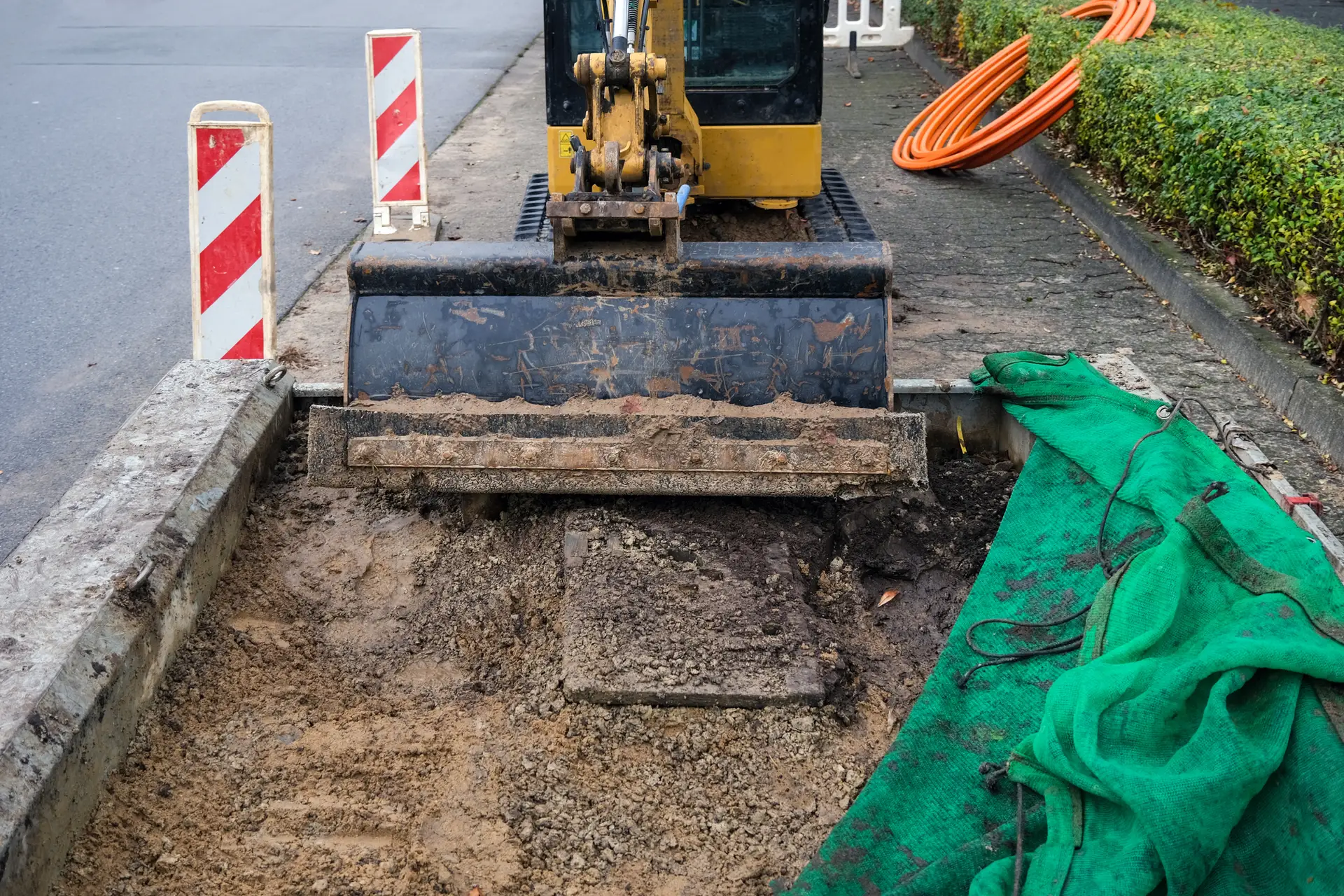 Concept of Construction Site: Low angle view of an Excavator on a Road with Warning Barrier, fiber optic cable and plenty of Copy Space in the Foreground, Selective Focus