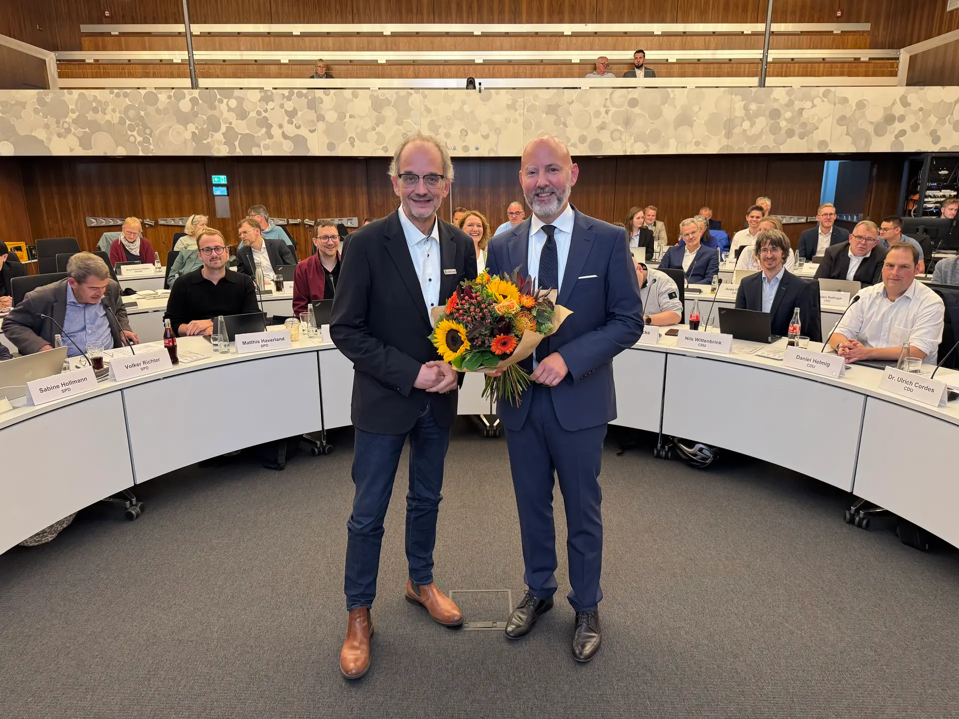 (v.l.) Bürgermeister Matthias Trepper beglückwünscht Henning Matthes mit einem Blumenstrauß, der in seinem Amt als Beigeordneter der Stadt Gütersloh bestätigt worden ist und weitere acht Jahre Beigeordneter für die Bereiche Bildung, Jugend, Soziales und Sport bleibt.