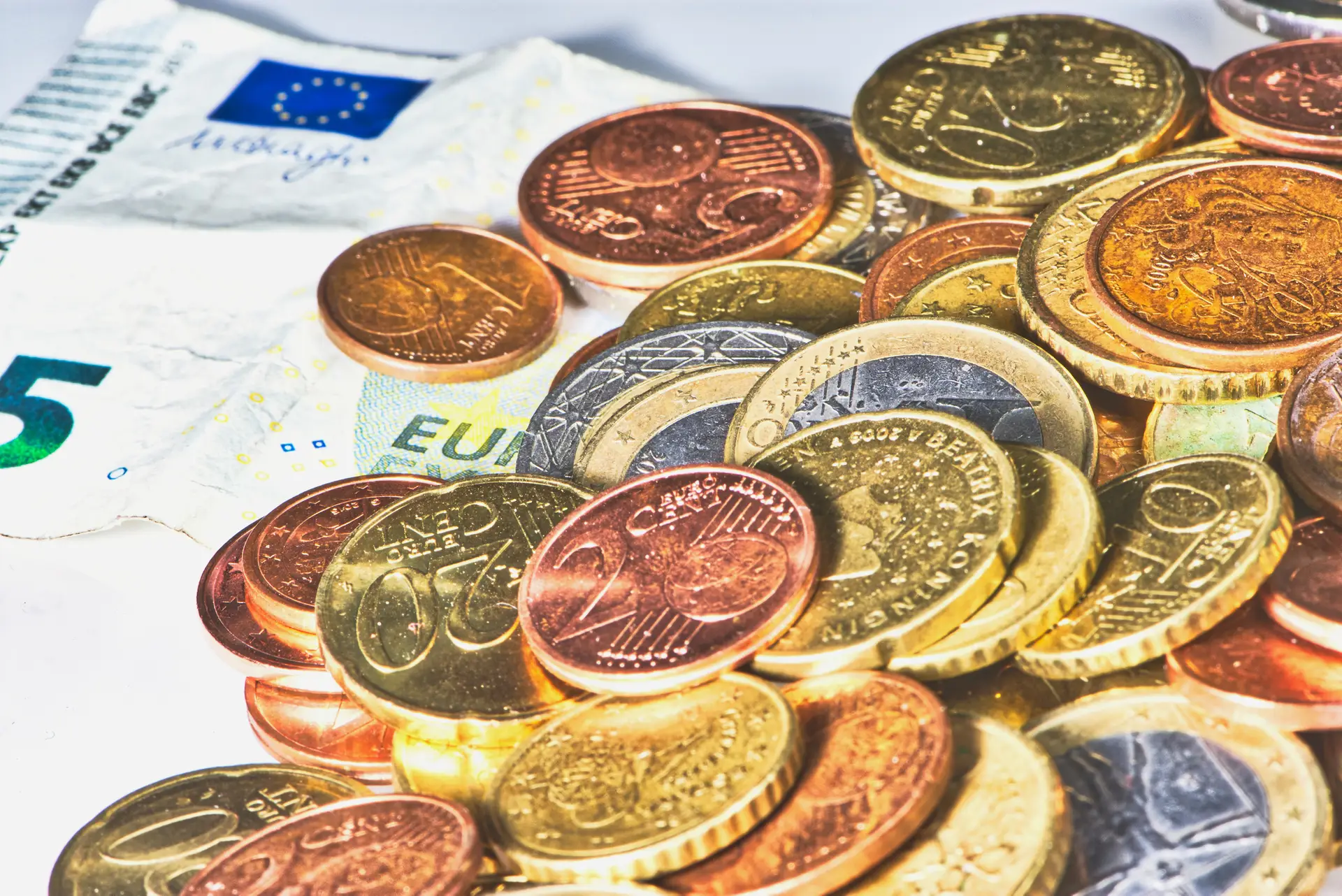 pile of Euro coins and cent coins beside five Euro banknote