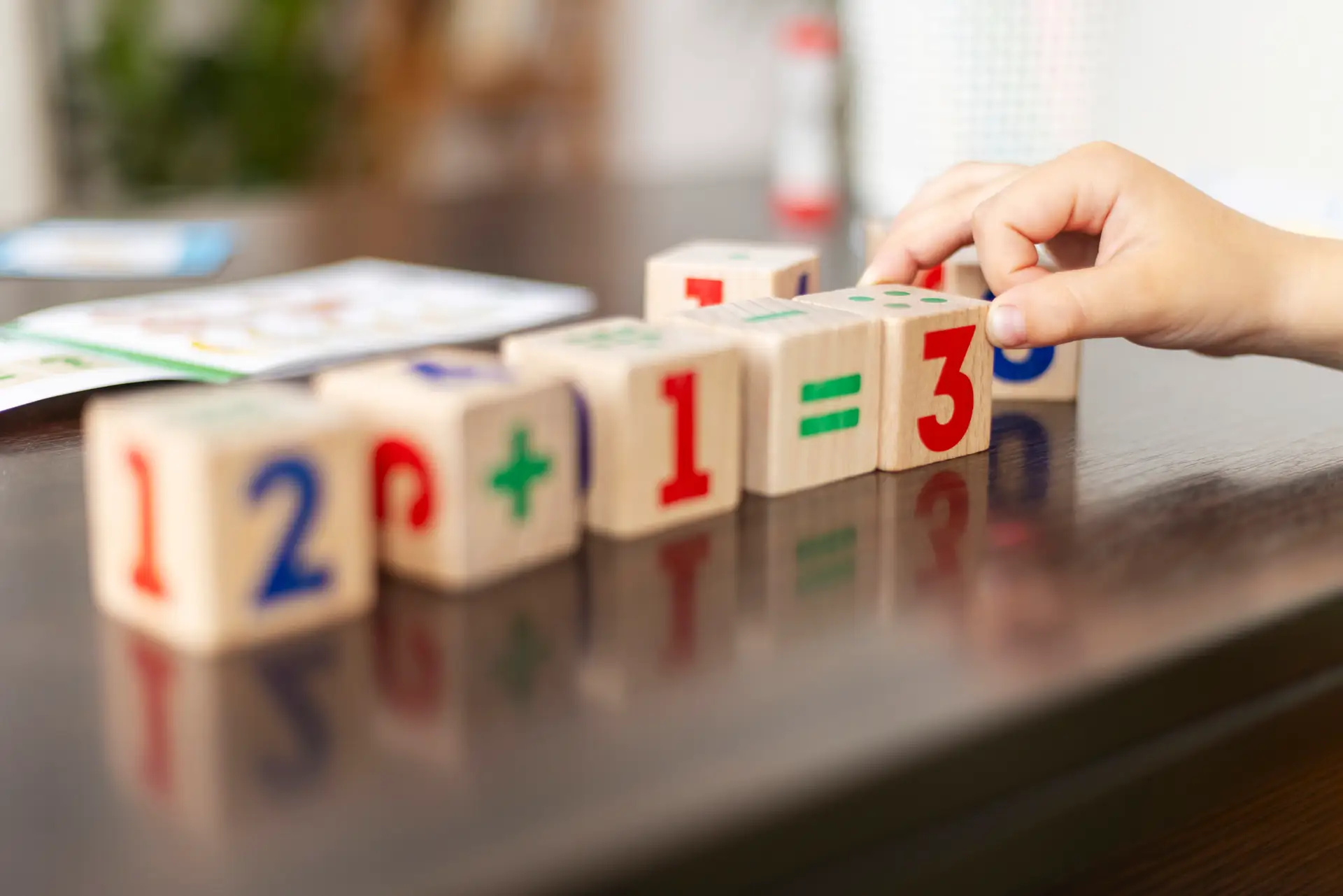Child arranging wooden blocks with numbers and math symbols on a table. Educational activity focusing on basic arithmetic. Close-up of hands and blocks