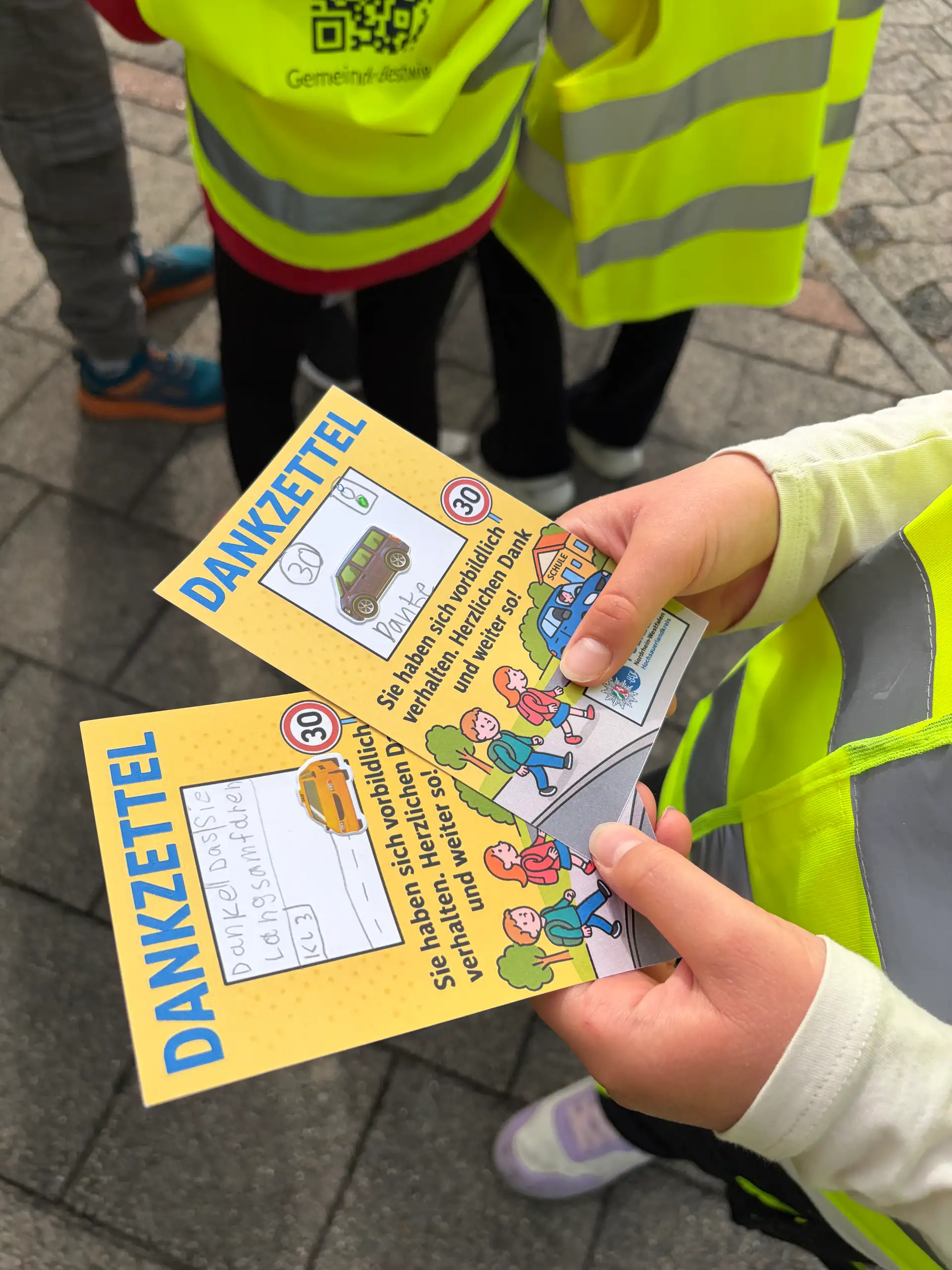 Bildzeile: Dank- und Denkzettel verteilen Kinder gemeinsam mit der Polizei an Autofahrerinnen und Autofahrer.