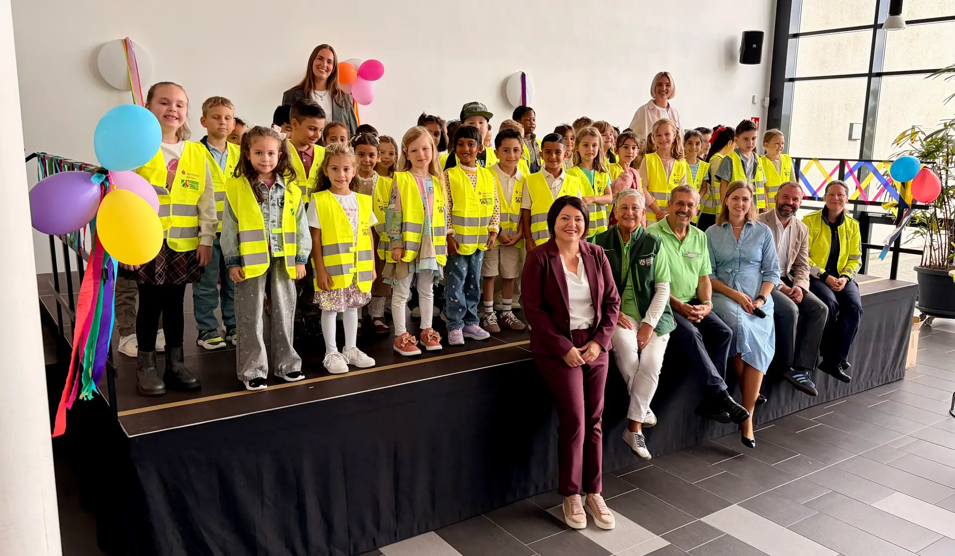Sichtbar und sicher unterwegs: Die Erstklässler der GGS Annapark präsentieren stolz ihre neuen Warnwesten gemeinsam mit Sparkassen-Gebietsdirektorin Sonja Alagic (vorne), Schulleiterin Katja Ritter-Ott, Bürgermeister Tim Krämer sowie Vertretern von Verkehrswacht und Polizei Aachen.
