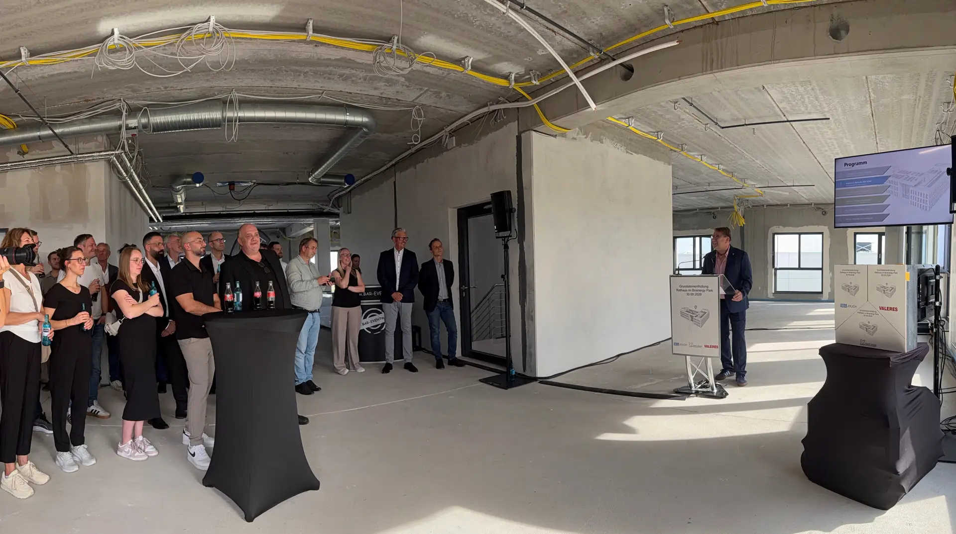 Mehrere Personen bei einer Veranstaltung anlässlich der Grundsteinenthüllung für ein neues Rathaus in einem Veranstaltungsbereich im Brainergy Park.