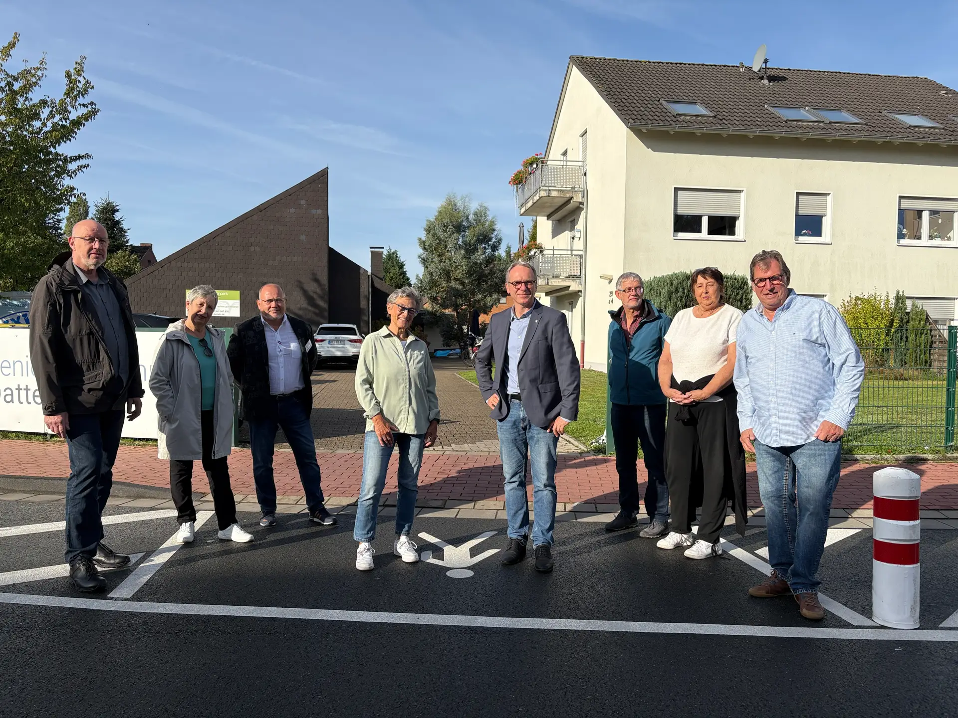 Acht Personen stehen gemeinsam an einer Straßenquerung vor dem Seniorenwohnpark.