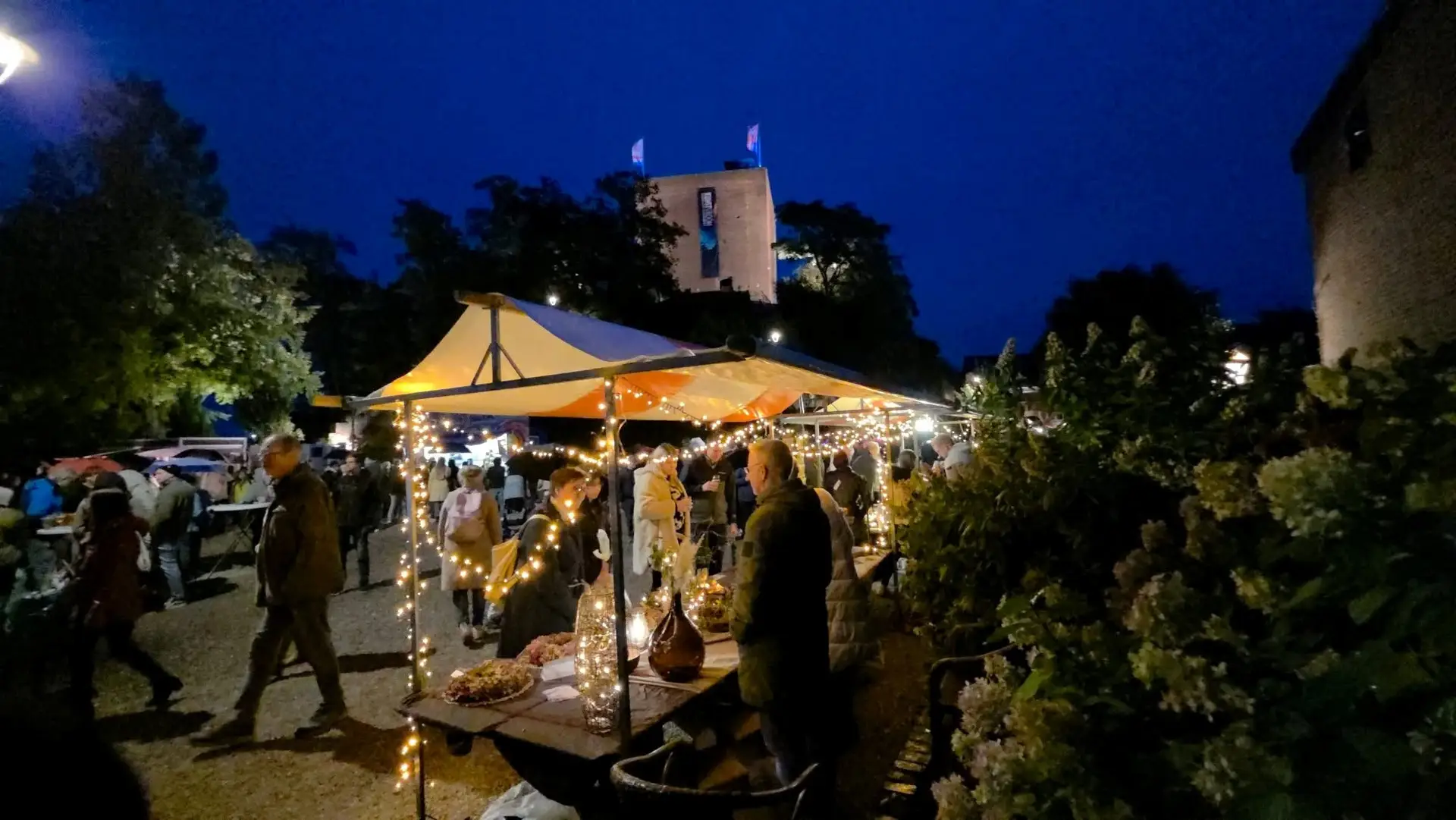 Besucherinnen und Besucher zwischen beleuchteten Marktständen an der Burg Wassenberg bei Dunkelheit.